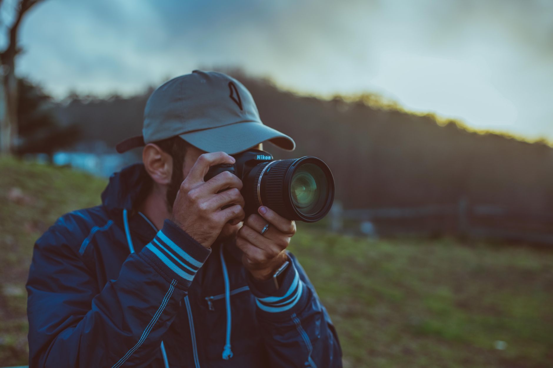 A man with a camera captures the serene outdoor landscape at sunset, highlighting a moment of focus and passion.