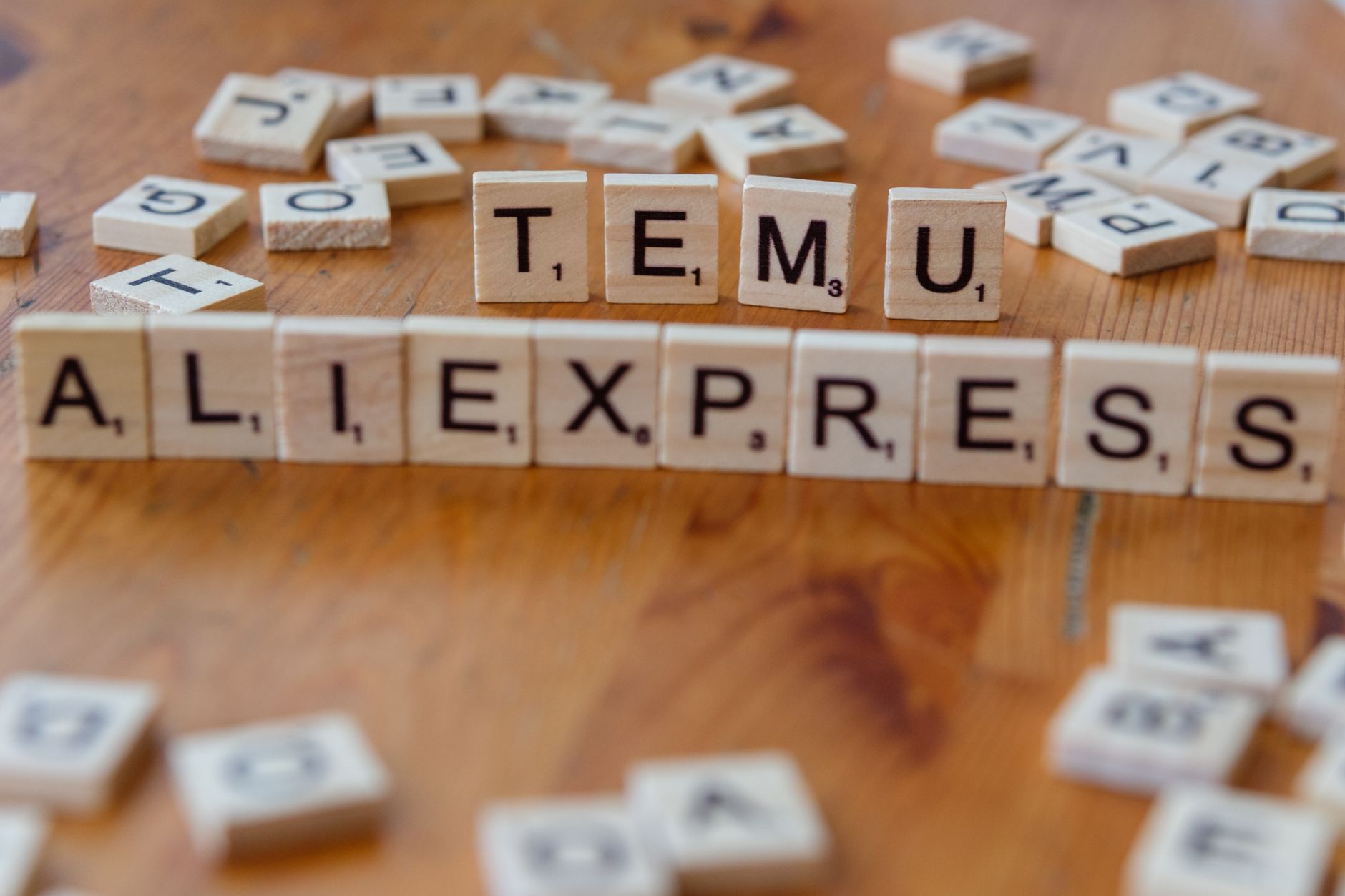 Close-up of Scrabble tiles on a wooden surface spelling 'TEMU' and 'ALIEXPRESS' amid scattered letters.